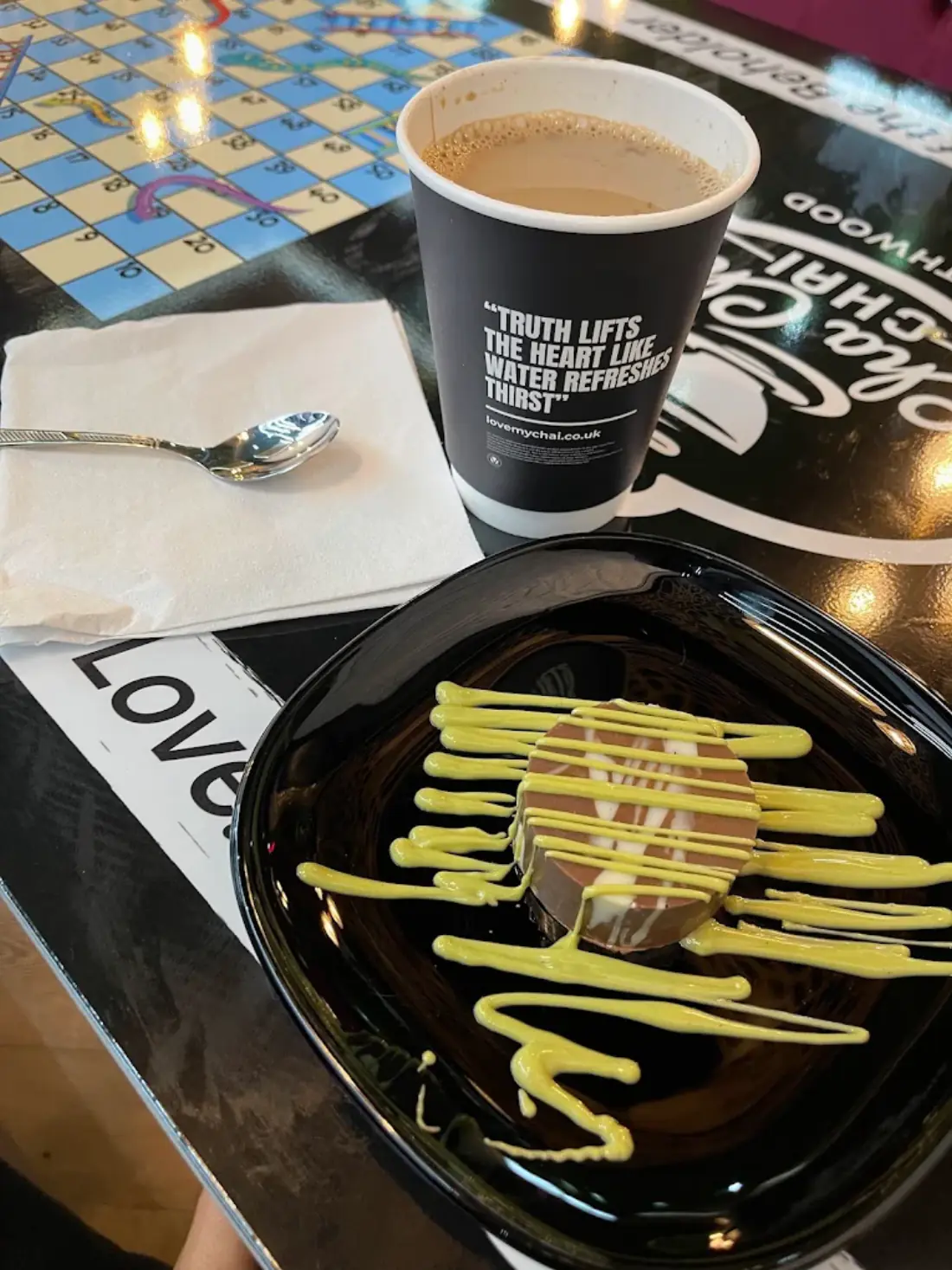 Karak chai in a branded Cha Cha Chai cup on a games table