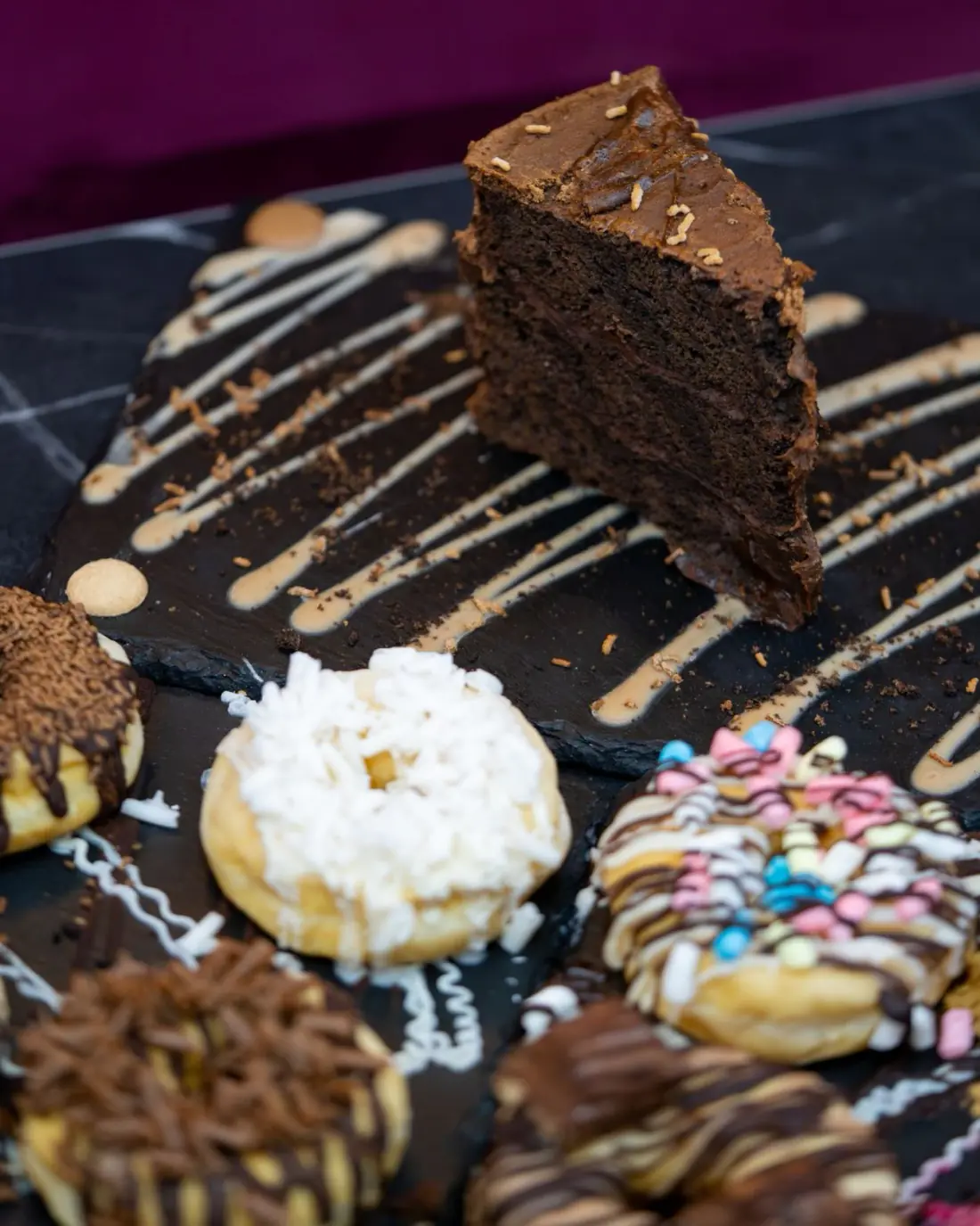 Chocolate cake and a spread of decorated donuts on a slate board