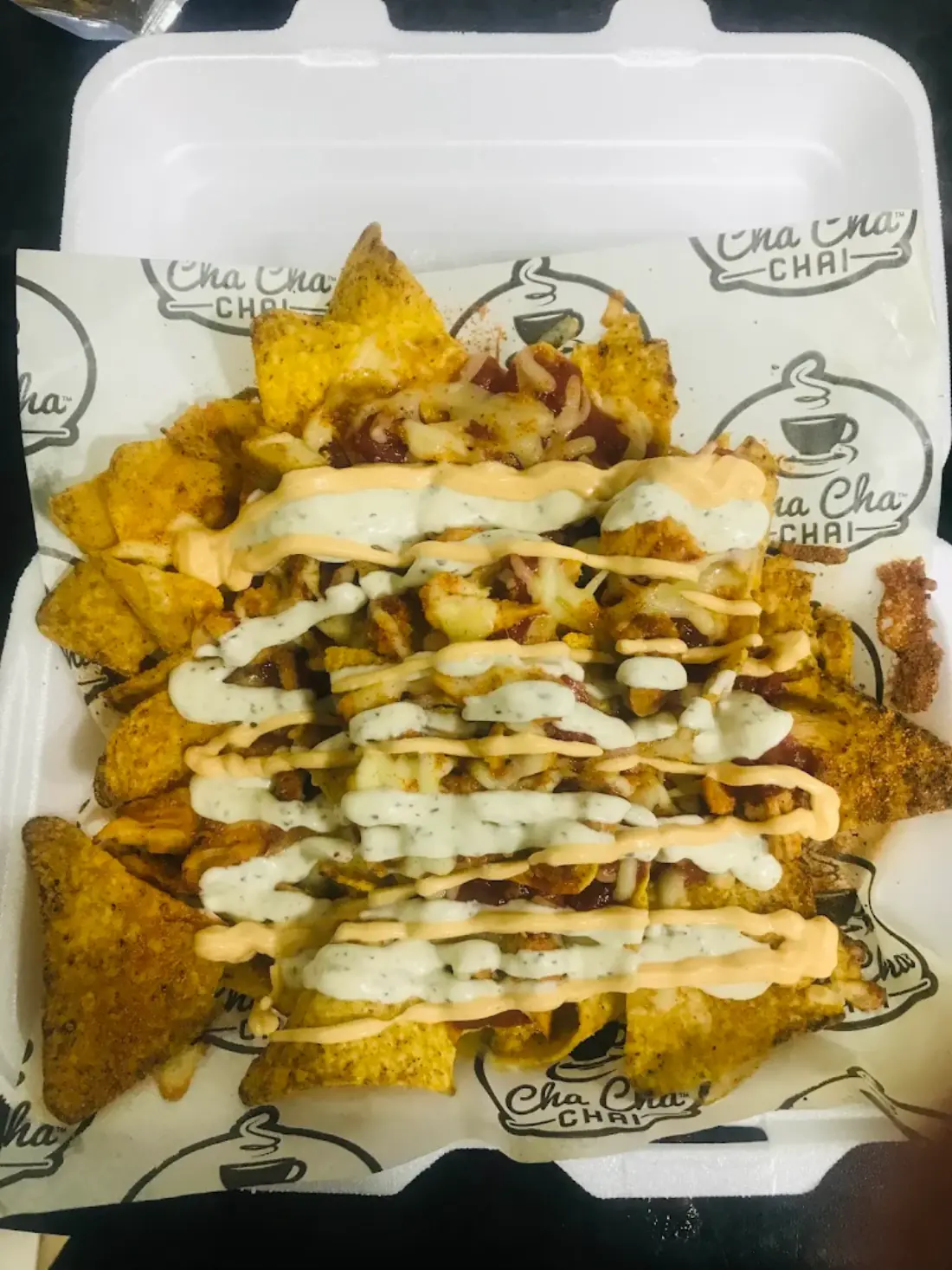 A takeaway box of loaded chips with cheese and house sauces on Cha Cha Chai Northwood Hills branded paper