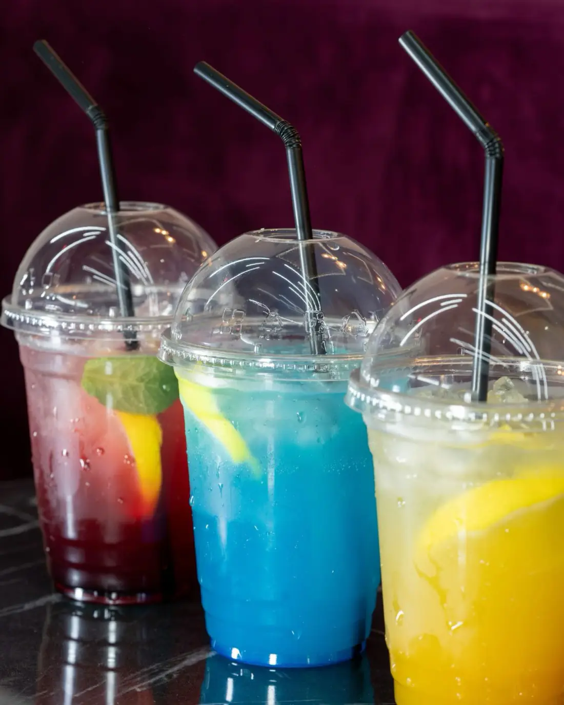 Three mocktails in domed cups against a deep magenta backdrop