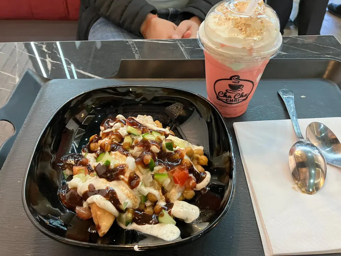 Samosa chaat layered with chutneys beside a pink chai shake