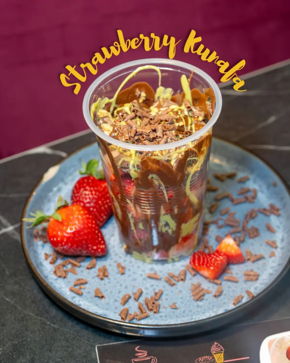 A Strawberry Kunafa Cup at Cha Cha Chai Northwood Hills, layered with strawberries, chocolate and shredded pastry, served on a plate with chocolate curls