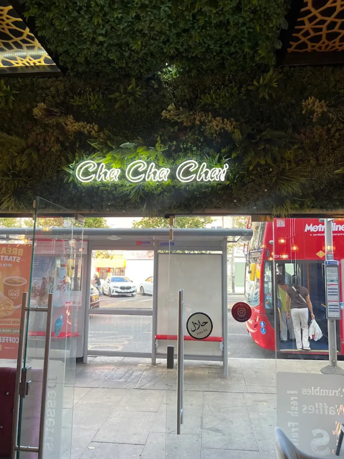 The neon Cha Cha Chai sign glowing on the foliage wall above the entrance